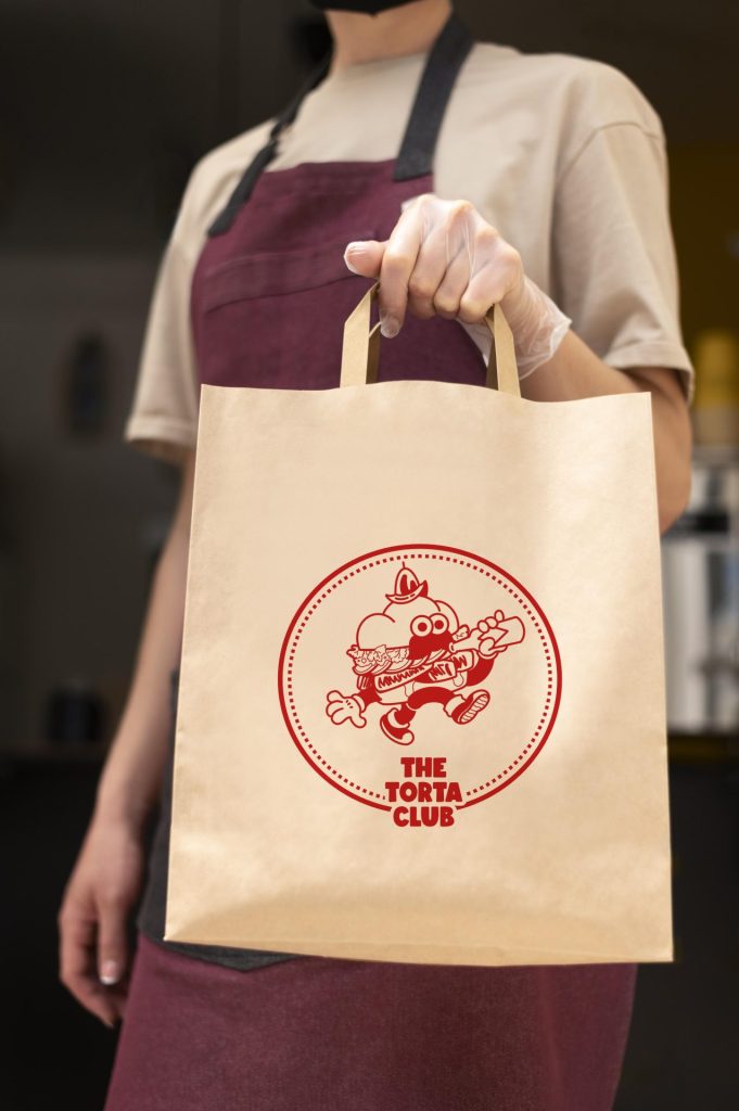 A restaurant worker, wearing a maroon apron, holds a paper bag by the handle.